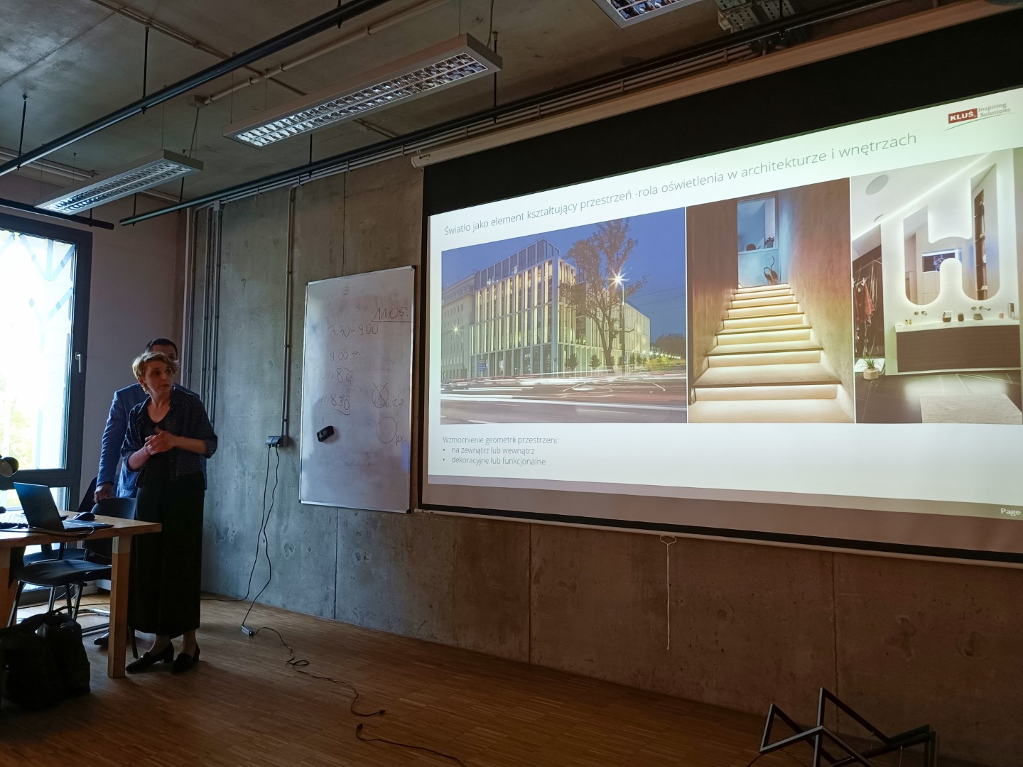 Prowadzący spotkanie stoją przy ekranie prezentacyjnym