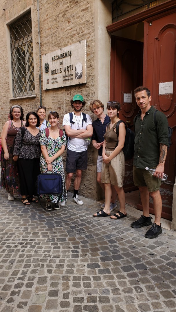 Grupa studentów pozuje do zdjęcia na uliczce przed wejściem do Academia di Belle Arti