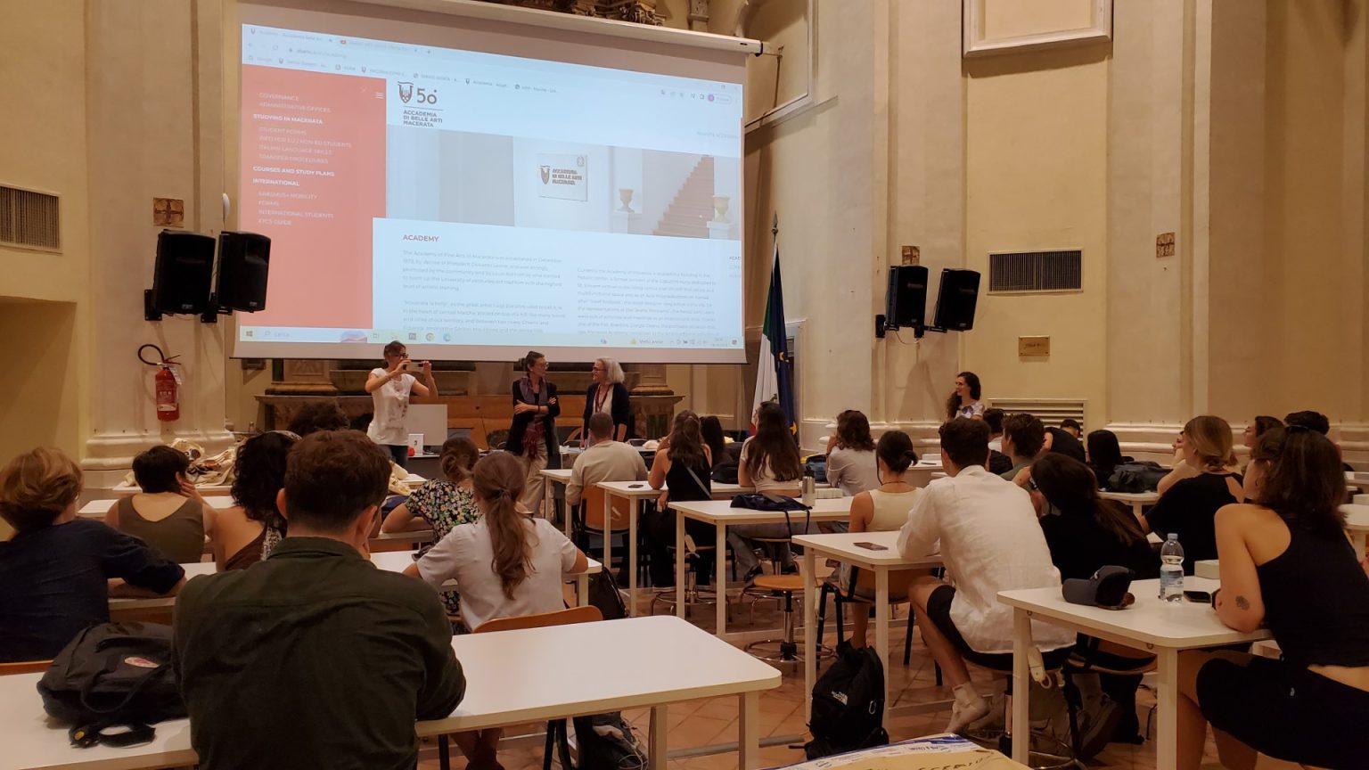Studenci na sali wykładowej, oglądają wyświetlaną na dużym ekranie prezentację Academia di Belle Arti Macerata