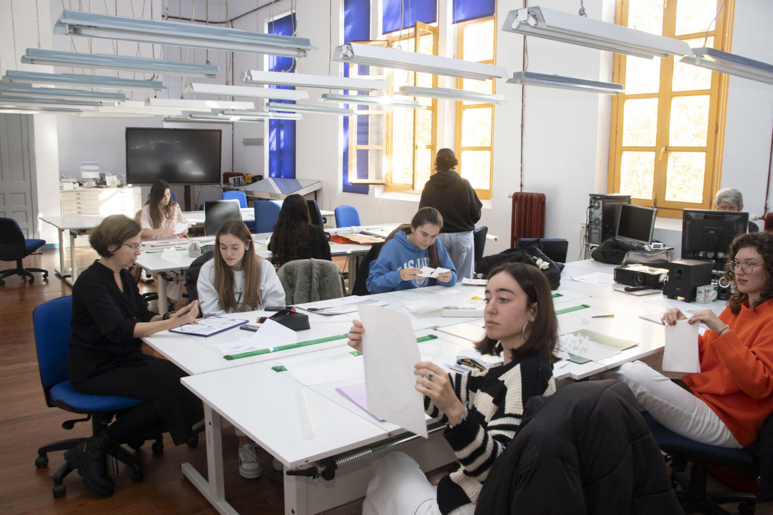 Fotografia w dniu trwania warsztatów. Studenci wraz z prowadzącą zajęcia projektują kompozycje z papieru w jednej z sal uczelni ESDIR.