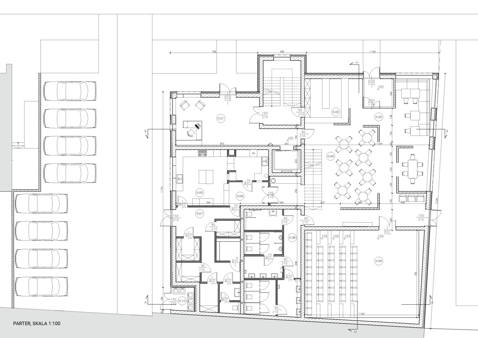 To jest rzut parteru budynku w skali 1:100. Plan obejmuje restaurację z salą kinową, kuchnią, strefą sanitarną i przestrzenią gastronomiczną z rozmieszczonymi stolikami. Widać także klatkę schodową, pomieszczenia pomocnicze i wejścia. Po lewej stronie znajduje się parking dla samochodów.