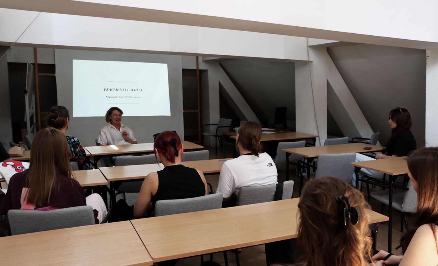 Zdjęcie przedstawia grupę studentów oraz prowadzącą, podczas wykładu wprowadzającego do warsztatów Fragmenty Całości.